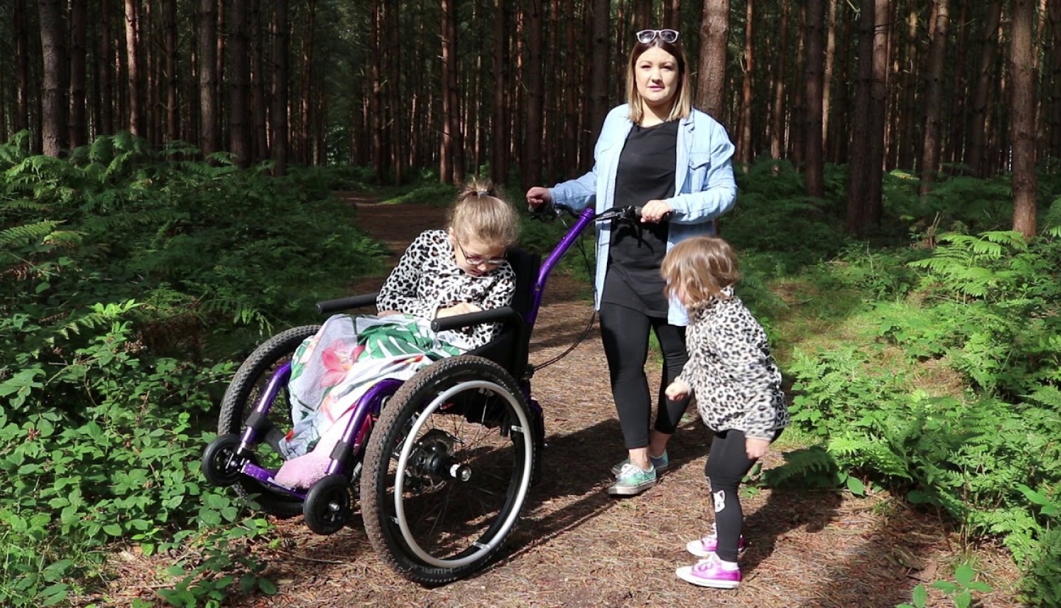 Pieaugušais stumj bērnu ratiņkrēslā pa meža taku